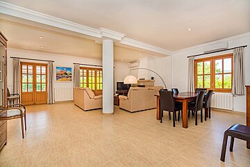 A spacious, bright open-plan living and dining room with beige sofas, a wooden dining set, tiled floors, and large windows.