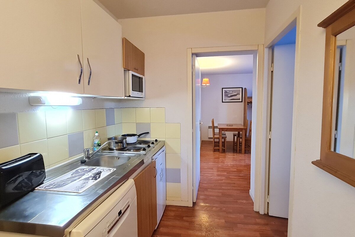 A compact kitchen with a sink, stove, and microwave, opening to a dining area featuring a wooden table and chairs, connected by a doorway.