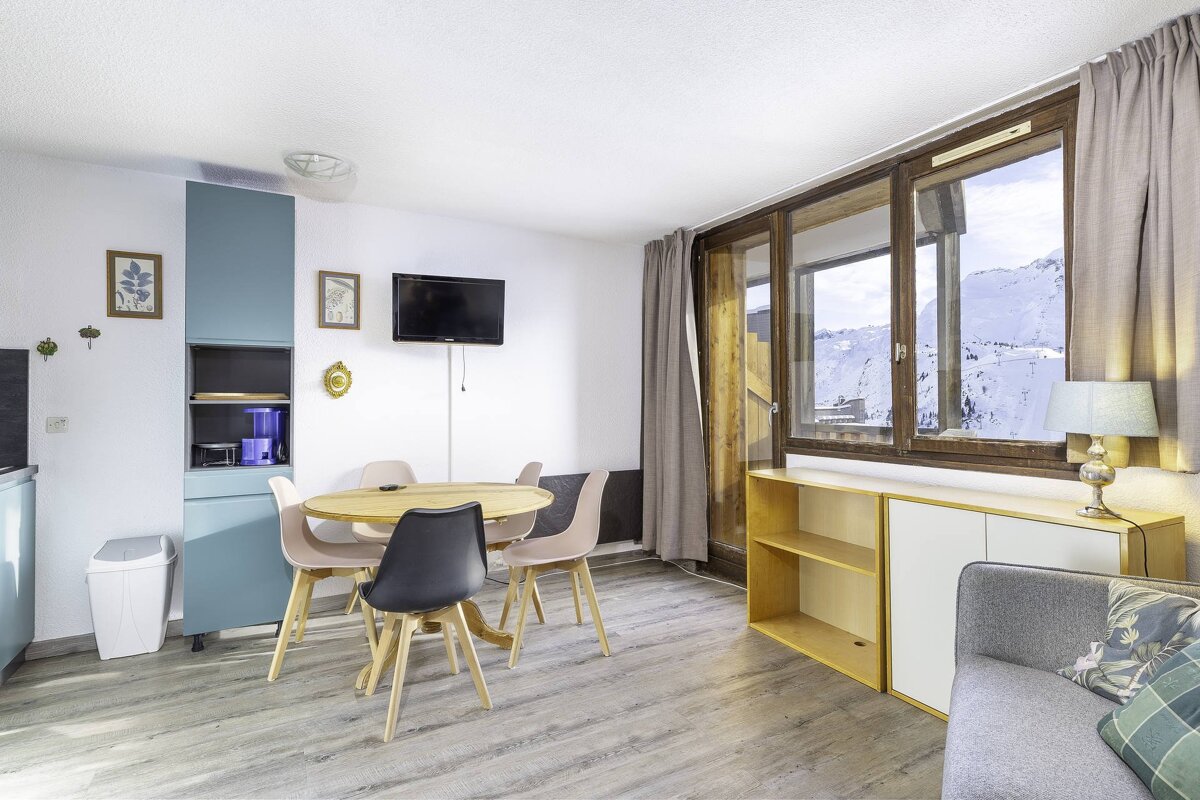 Modern apartment living/dining room with a table, TV, and a stunning snowy mountain view from the large window.