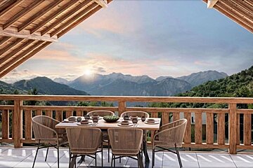 A scenic wooden balcony dining area with a table set for six, offering a breathtaking view of mountains at sunset.