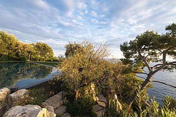 A swimming pool surrounded by trees and rocks overlooking the ocean