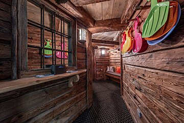 Rustic wooden hallway with colorful plastic sleds, a barred window, bench seating, and a hexagonal patterned floor, giving a cozy cabin feel.