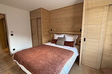 Cozy cabin-style bedroom with light wood paneled walls, matching closets, and a bed with a textured rust-colored throw blanket.