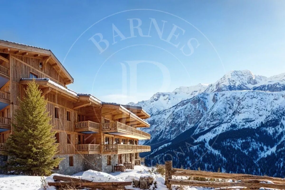 A grand wooden chalet with balconies sits in a snowy mountain landscape under a clear blue sky. A sparse evergreen and rustic fence are visible.