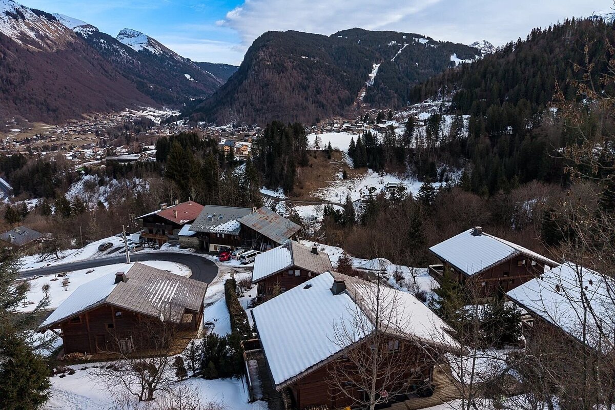 Snow-covered wooden chalets on a hillside overlooking a scenic alpine valley in winter.