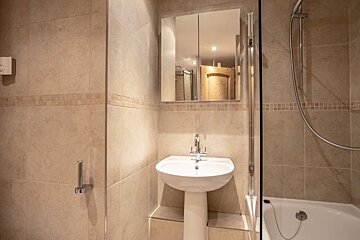 Modern beige-tiled bathroom featuring a white pedestal sink, mirrored cabinet, and a bathtub with a shower attachment.