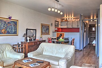 Cozy living room with cream leather sofas, a wooden coffee table, and a dining area with a kitchen in the background.
