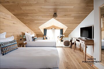 A stylish attic room with two single beds, extensive wood-paneled walls and ceiling, a diamond-shaped window, TV, and desk.