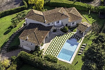 High-angle view of a luxury home featuring a tiled roof, a swimming pool, patterned patio, and lush green lawns.