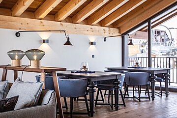 Cozy dining area with exposed wooden ceiling beams, dark tables, blue chairs, and stylish modern lighting.