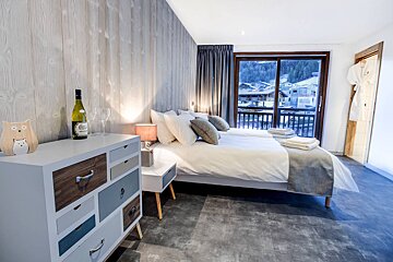 A bottle of wine sits on a dresser next to a bed