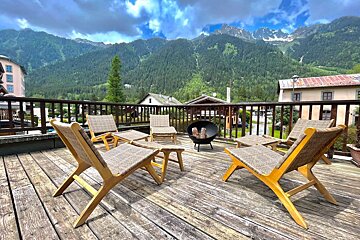 A deck with chairs and a fire pit with mountains in the background