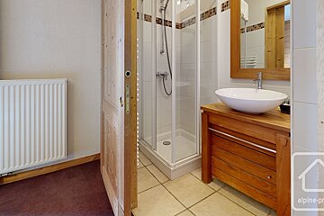 A modern bathroom featuring a wooden vanity with a white vessel sink, a glass shower stall, and light-colored tile floors.
