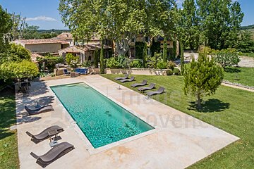 A large swimming pool is surrounded by lawn chairs and a large house