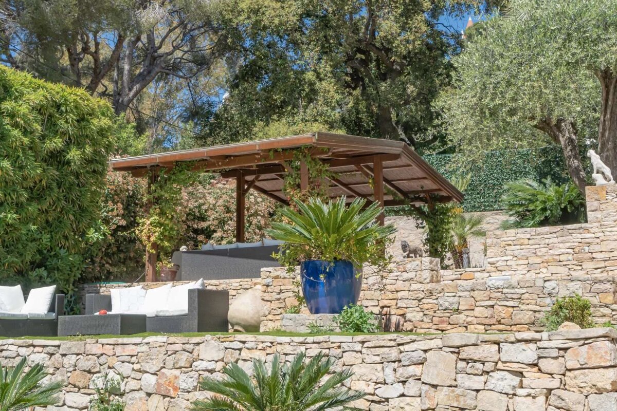 A stone wall with a pergola and a blue potted plant