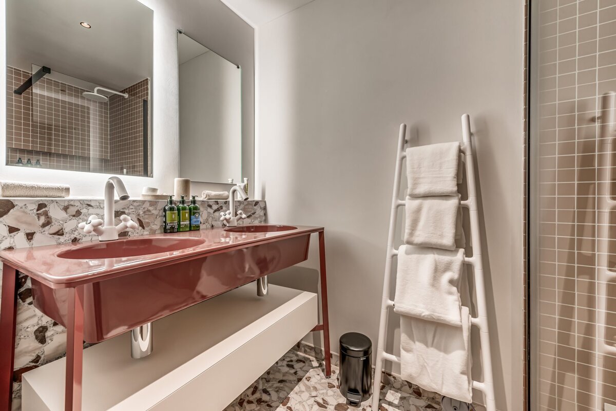 Modern bathroom featuring a stylish reddish-pink double vanity, terrazzo tiling, backlit mirrors, and a white ladder towel rack.
