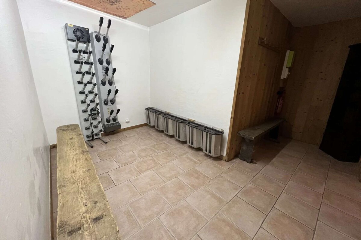 A ski locker room featuring two boot drying racks, long wooden benches, a row of boot warmers, and light-colored tiled flooring.