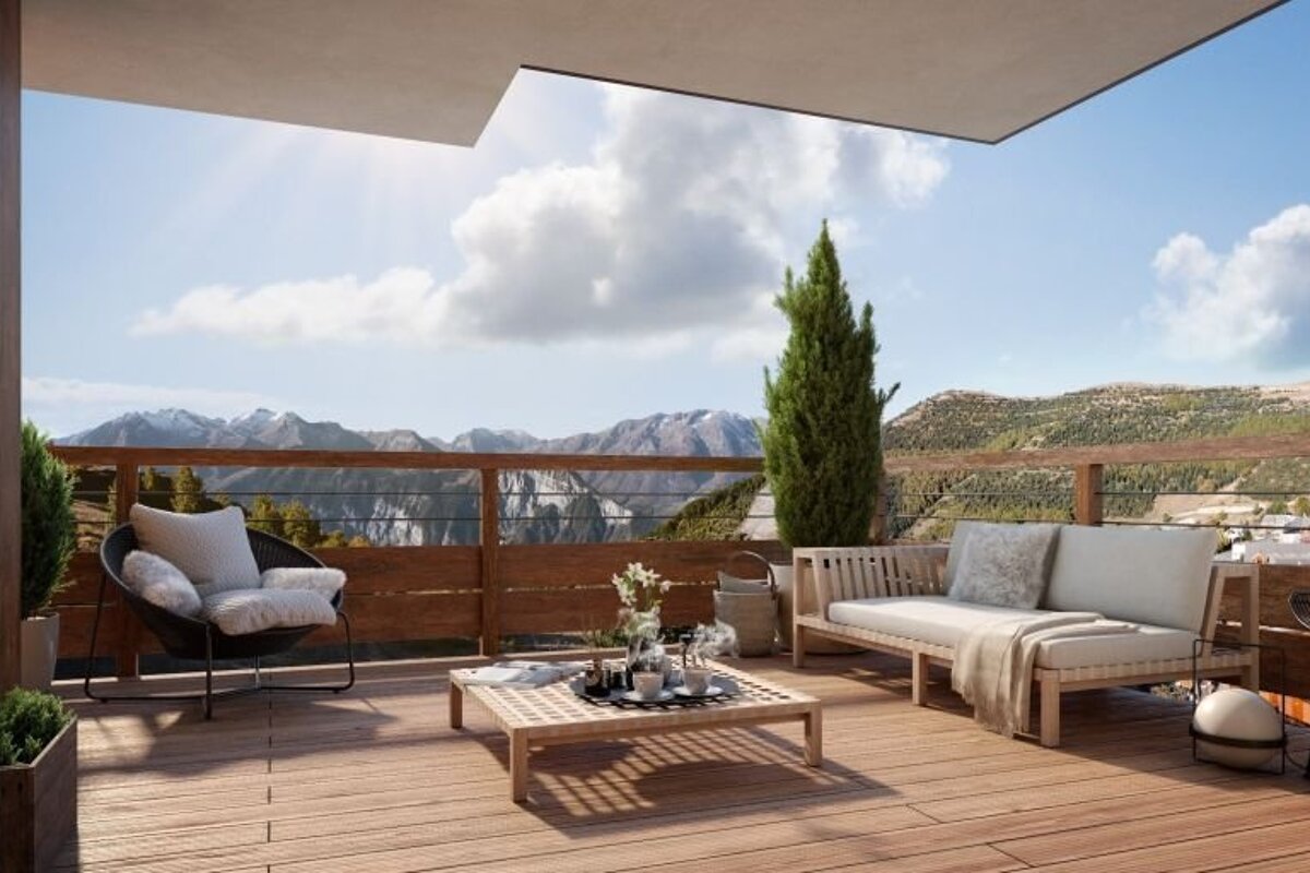 A cozy wooden balcony with comfortable patio furniture overlooking a stunning mountain range on a sunny, cloud-filled day.