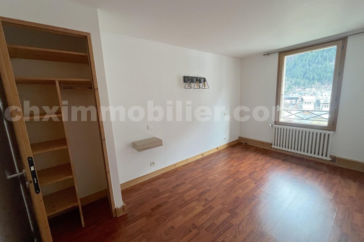 Empty room with wooden floor, white walls, built-in closet, window with mountain town view, radiator, and a wall shelf.