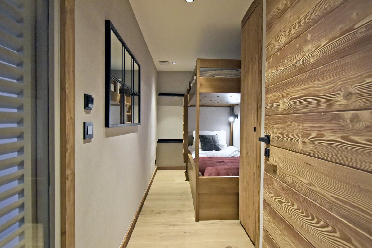 A narrow hallway with a wooden paneled wall leads to a cozy alcove featuring wooden bunk beds.