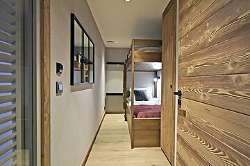 A narrow hallway with a wooden paneled wall leads to a cozy alcove featuring wooden bunk beds.