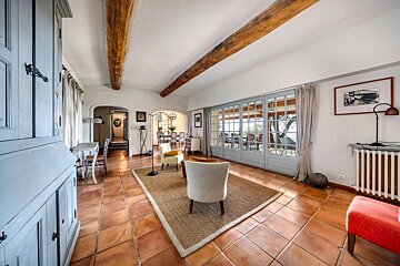 A bright, rustic living space with terracotta floors, exposed wooden beams, French doors to a patio, and an adjoining dining area.
