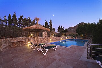 A swimming pool with a thatched umbrella and chairs