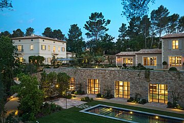 Luxurious Mediterranean estate at dusk with a grand villa, tiered gardens, and an illuminated pool.