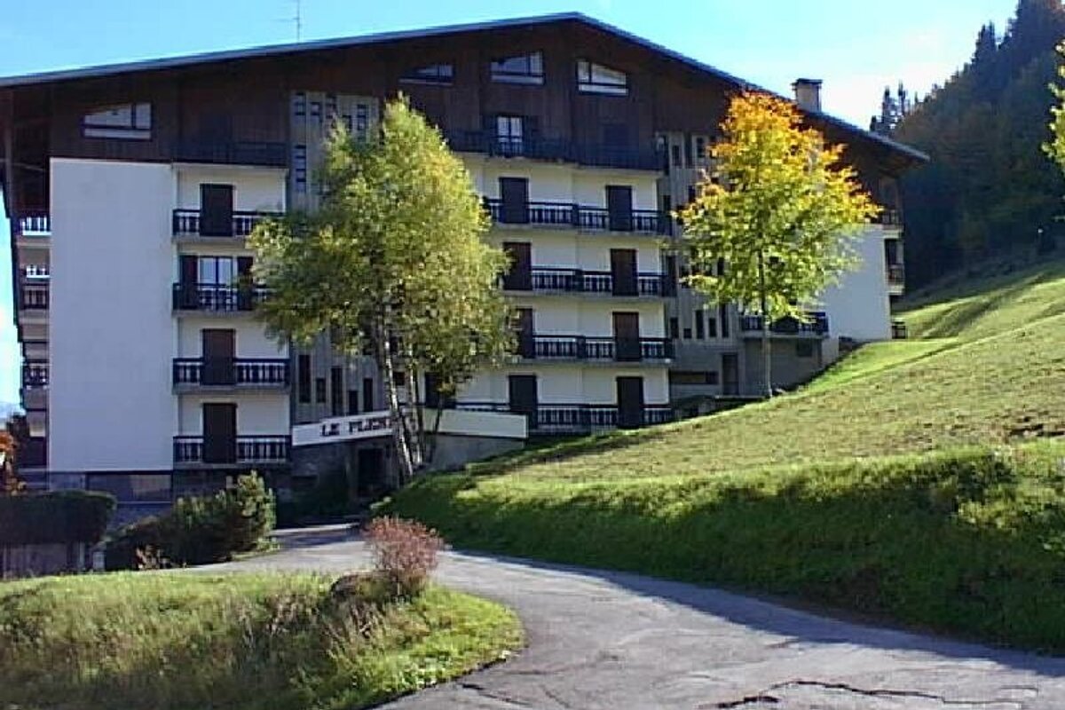 A multi-story chalet-style lodge situated on a grassy hill next to autumn trees and a paved driveway.