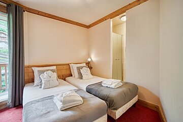 A cozy twin bedroom with white robes & towels on beds, wooden accents, and red carpet. A window overlooks greenery, and a shower stall is visible.
