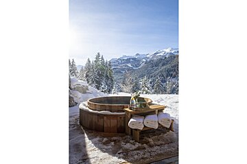 A wooden hot tub in the snow with mountains in the background