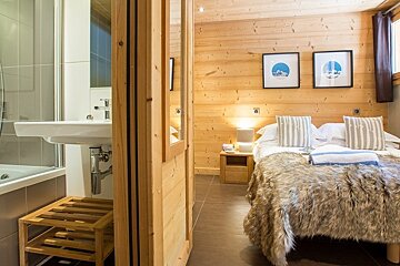 Cozy wooden cabin bedroom with a fur-covered bed next to a modern bathroom sink.