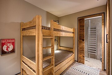Cozy, rustic room with wooden bunk beds, checkered bedding, a mountain sign, and an open sliding door to a modern bathroom.