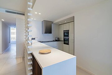 A modern, minimalist white kitchen featuring a large island, stainless steel appliances, and a slatted partition wall.
