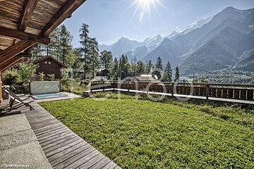 A hot tub sits on a lush green lawn with mountains in the background