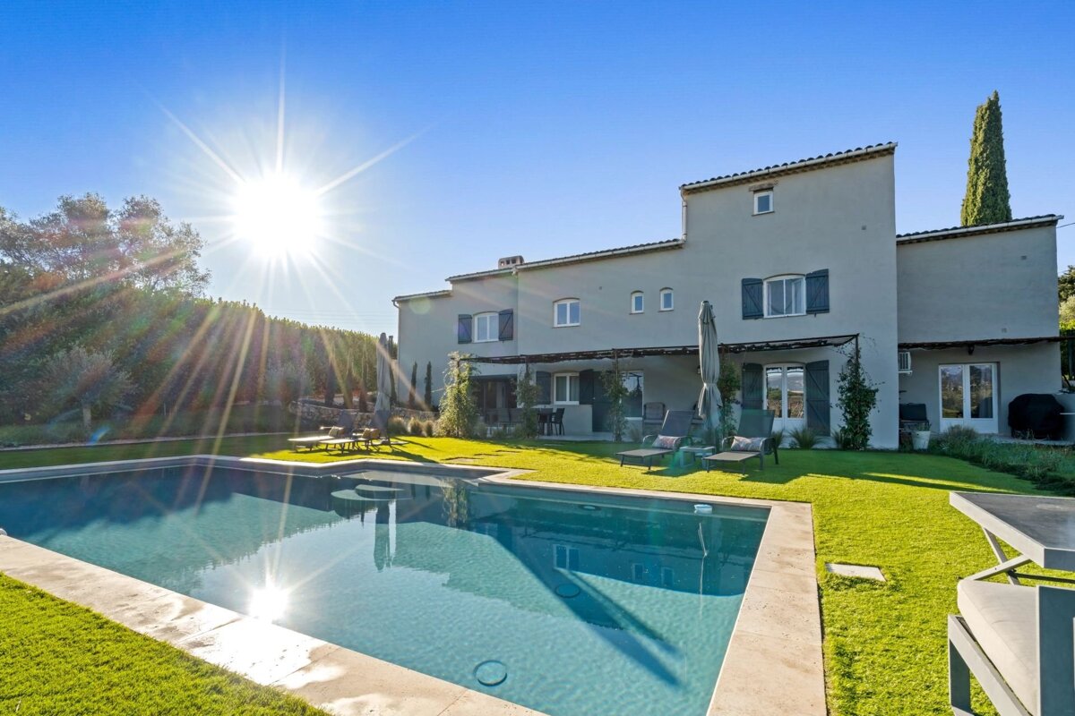 Luxurious villa featuring a sparkling swimming pool, lush green lawn, and sun loungers under a bright, sunny sky.