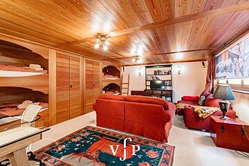 Cozy cabin-style room with a wood-paneled ceiling, built-in bunk beds, two red sofas, and a decorative rug.