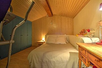 Cozy attic bedroom featuring wood-paneled walls, a bed with white linens, blue closets, and an exercise machine.