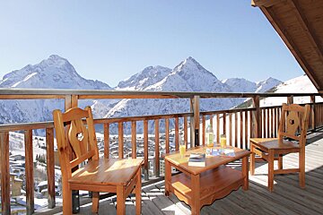 A balcony with two chairs and a table with mountains in the background
