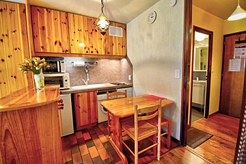 A cozy dining area with light wooden chairs and table, a kitchen pass-through, wood paneling, and a hallway entrance.