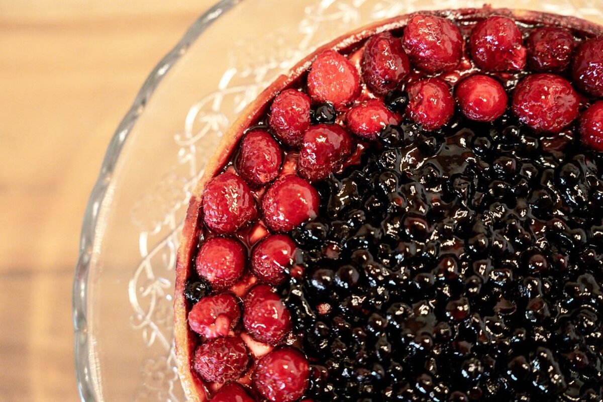 A vibrant berry tart featuring glazed red raspberries and dark blueberries, resting on an ornate glass platter.