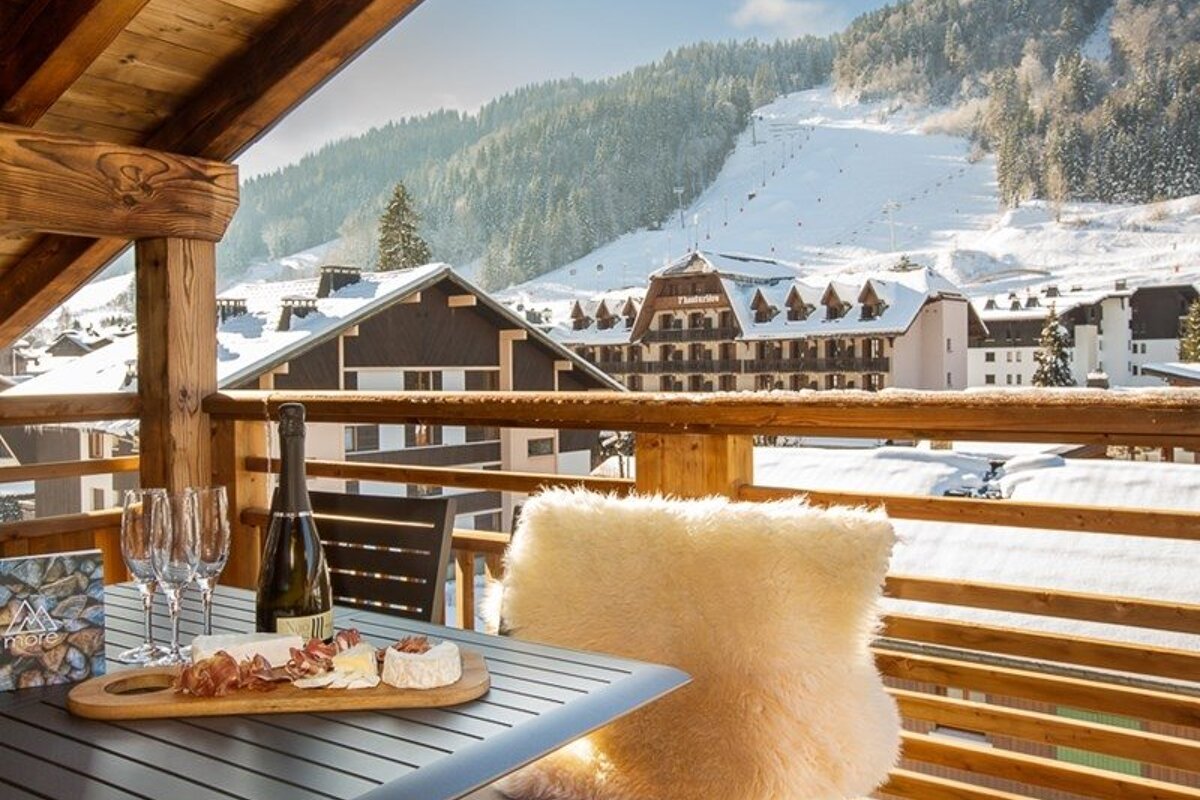 Wine and cheese on a cozy wooden chalet balcony overlooking a snow-covered alpine ski resort.