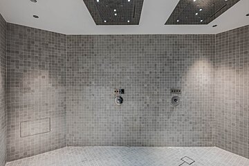 A shower with a gray tiled wall and two shower heads