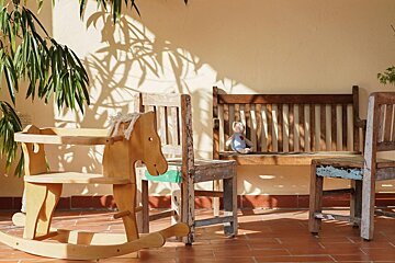 A teddy bear sits on a wooden bench next to a rocking horse
