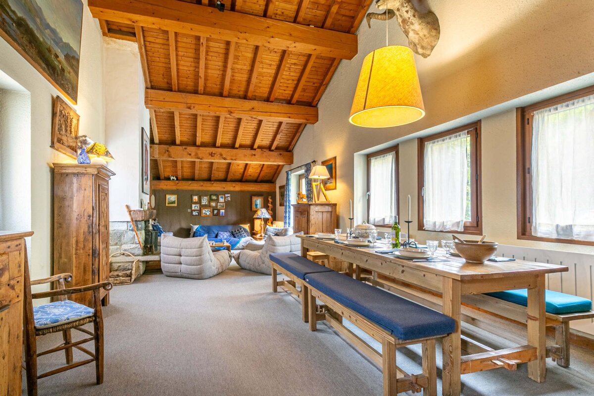 Cozy chalet interior featuring a long wooden dining table with blue benches under a vaulted, exposed-beam wooden ceiling.
