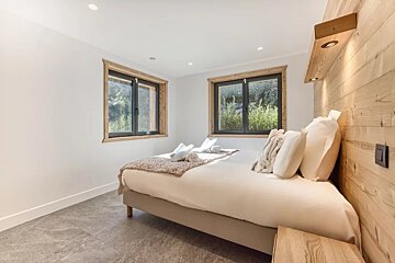 Cozy, modern bedroom with a white-dressed bed, two wood-framed windows, grey tile flooring, and a light-wood paneled headboard wall.