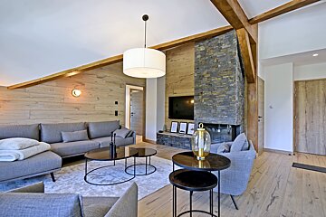 Modern living room with wood paneled walls, exposed beams, stone fireplace, gray sofas, and contemporary lighting.