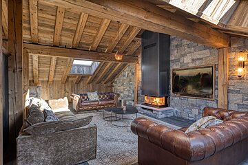Cozy rustic cabin living room featuring exposed wood ceilings, a stone wall fireplace, and brown leather Chesterfield sofas.