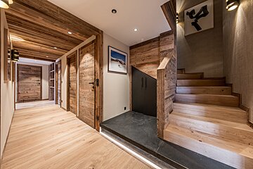 Warm, rustic wooden hallway and staircase in a chalet home, featuring timber walls, doors, ceilings, and light wood floors with ambient lighting.