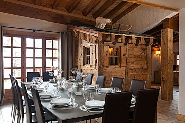 Rustic chalet dining room with a long, set table and an indoor wooden cabin adorned with a polar bear and sled on its roof.